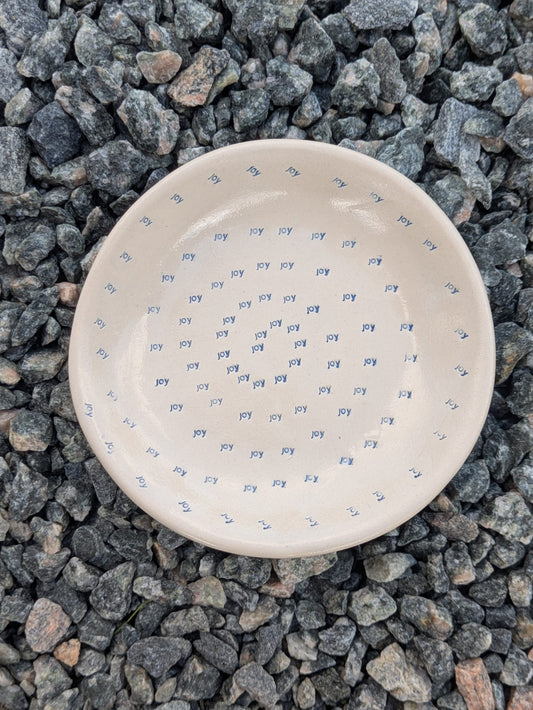 Joy Spiral round trinket tray – a handmade ceramic dish about 10.5cm wide, decorated with a hand-stamped dotted spiral, shown from above on grey stone chippings