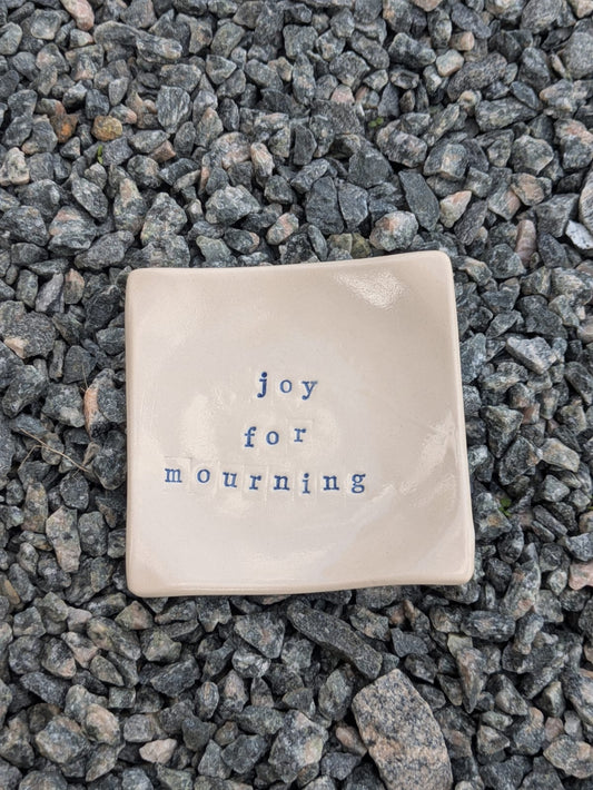Joy for Mourning square trinket tray – a handmade ceramic dish about 9.5cm square, hand-stamped with the words “joy for mourning”, shown from above on grey stone chippings