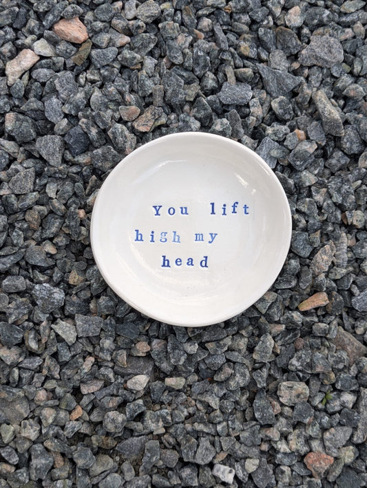 You Lift High My Head round trinket tray – a handmade ceramic dish about 10.5cm wide, hand-stamped with the words “you lift high my head”, shown from above on grey stone chippings